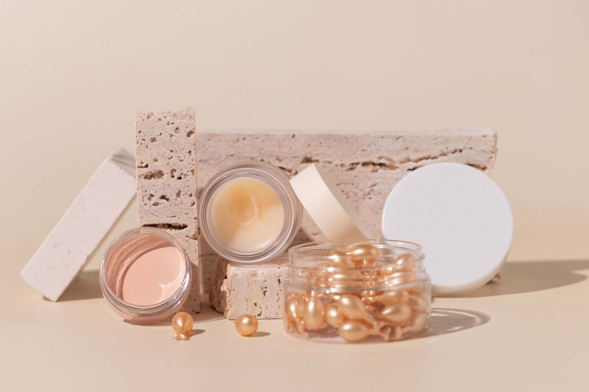 Opened cream jars on travertine stones on light beige close up, Cosmetic mockup